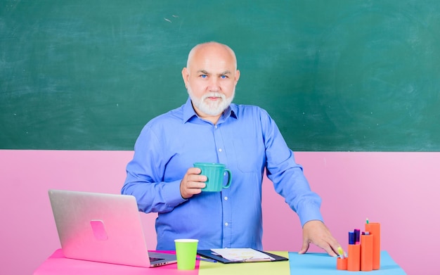 Foto pausa della lezione scolastica del professore universitario uomo maturo dell'insegnante con la tazza di caffè insegnante dell'uomo anziano con il notebook e il computer torna a scuola tutor del concetto di istruzione in classe prendere appunti