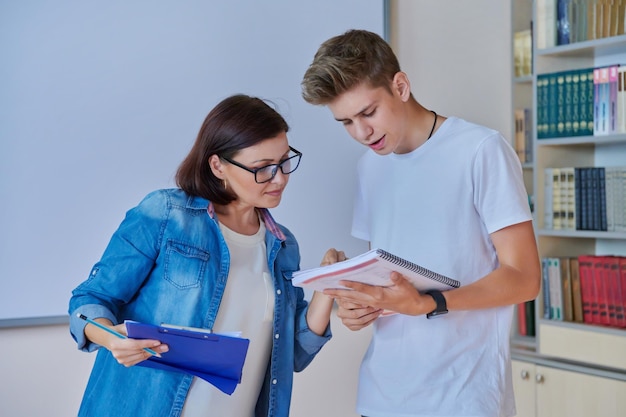 College student guy teenager meeting discussing with teacher mentor in classroom