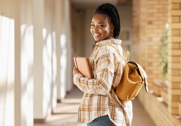 College student portret zwarte vrouw en universiteit met boeken en rugzak tijdens het wandelen op de campus Jonge generatie z vrouw blij met onderwijs, leren en toekomst na studeren aan schoolgebouw