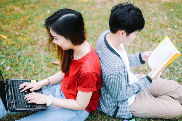 Foto studente di college che si siede con l'amico nel parco sull'erba verde con il computer portatile