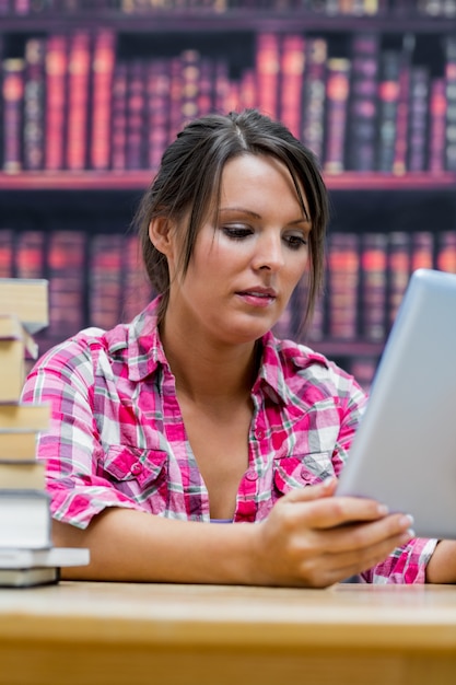 College student using digital tablet with stack of books at library