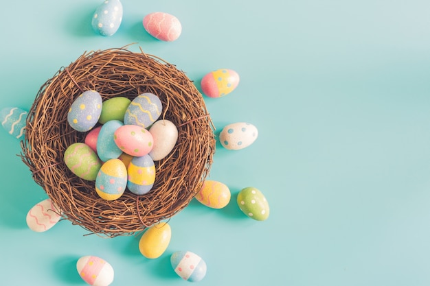 Coloeful easter eggs in nest on pastel color background with space.