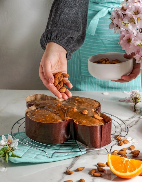 Colomba - traditional italian easter dove cake, process of decorating with hazelnut based glaze, macaranage, sprinkling with almonds,  woman shef hands.