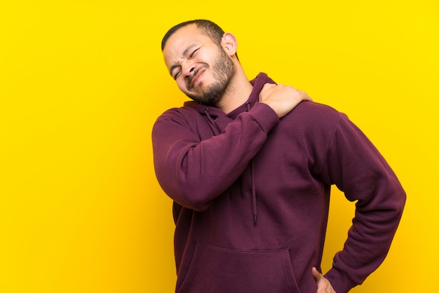 Colombiaanse man met sweatshirt over gele muur die lijden aan pijn in de schouder voor het hebben van een inspanning