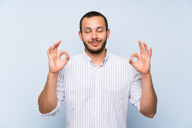 Colombiaanse man over geïsoleerde blauwe muur in zen pose