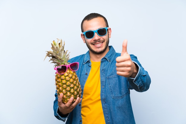 Colombiaanse mens die een ananas met zonnebril houdt die duimen op gebaar en het glimlachen geeft