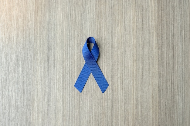 Photo colon cancer awareness, dark blue ribbon on wooden background