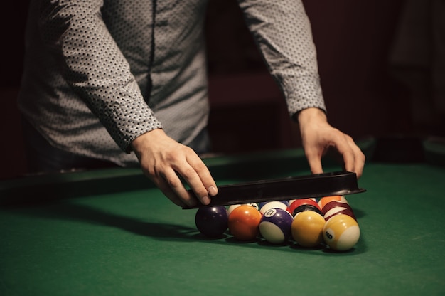 Color balls of american billiard in triangle on billiard table and billiard player close-up