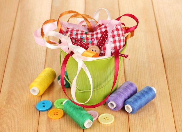 Color bucket with multicolor ribbons and thread on wooden background