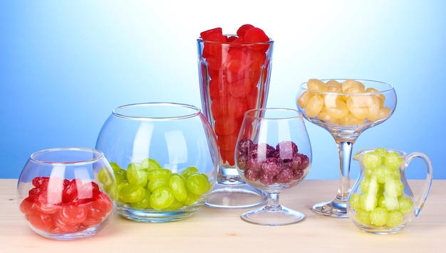 Photo color candies in glasses on wooden table on blue background