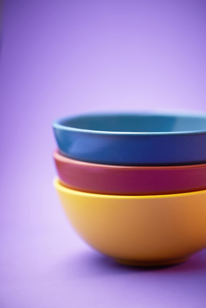 Color container and group of ceramic bowl kitchen equipment or plastic plate tower for soup cereal or breakfast food Colorful stack of blue yellow and maroon objects on purple background studio