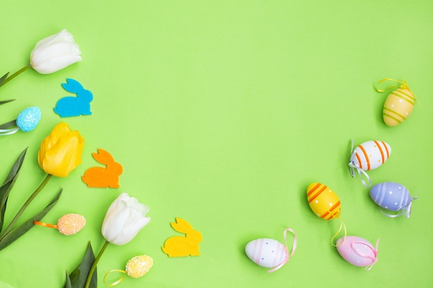 Color easter eggs and bunny with White, yellow tulips on a green background.