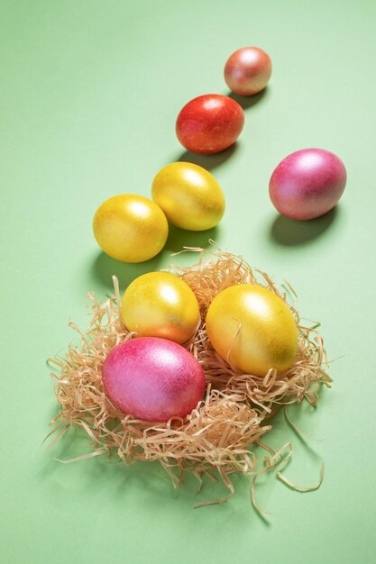 Color easter eggs is lying in nest made of straw and on green pastel background perspective view