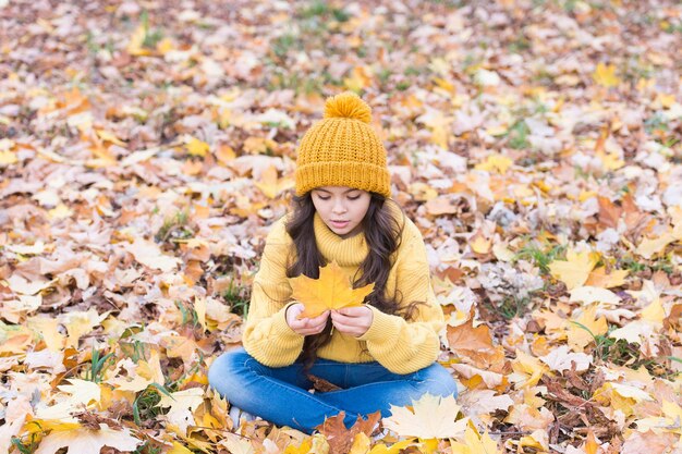 色は鮮やかです 小さな子供はカエデの葉を保持します 愛らしい小さな赤ちゃんは黄色の葉で遊ぶ かわいい小さな子供は秋の葉の上に座ります 屋外の秋のファッションスタイルの小さな女の子