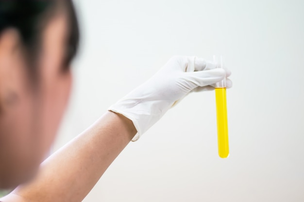 Photo color liquid in test tube hold in hand with glove of scientist isolated on the light plain wall