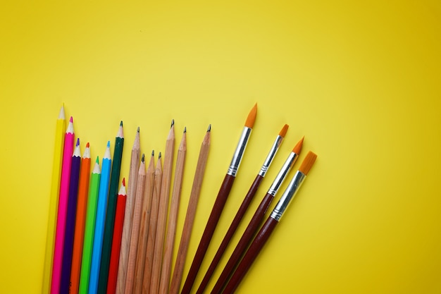 黄色の背景にカラー鉛筆とブラシ
