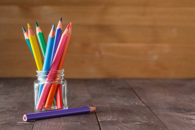 Color pencils in glass jar on wooden surface