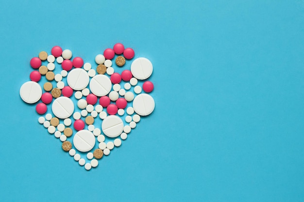 Color pills in the shape of a heart on a blue background Medicine concept