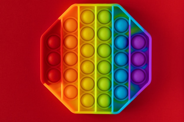 Color pop it antistress toy for children. rainbow octagon shaped isolated on red background . Pop it toy.