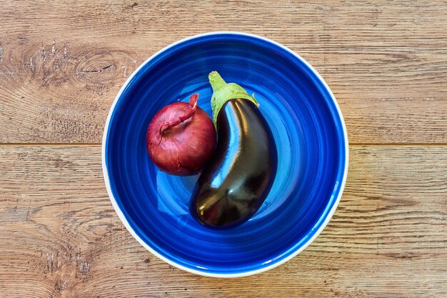 Color still life  purple bulb of red sweet onion and purple eggplant on a blue plate