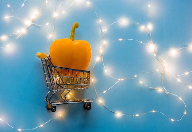 Color sweet pepper in supermarket cart with fairy lights on blue background