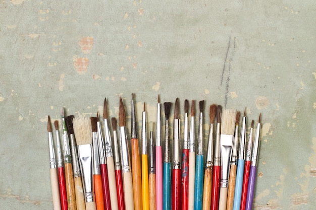 Colored artistic paintbrushes on a green wooden background with copy space