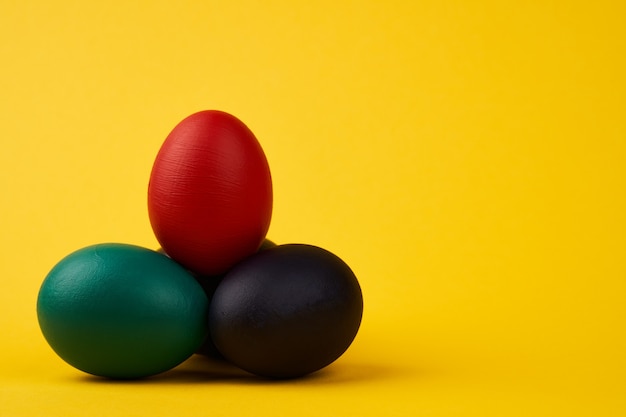 Colored black green blue red easter eggs on bright yellow background