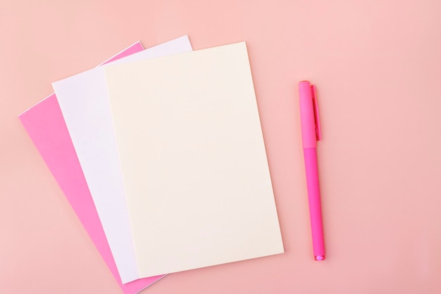 Colored blank sheets of pastel colors on a pink next to the pen