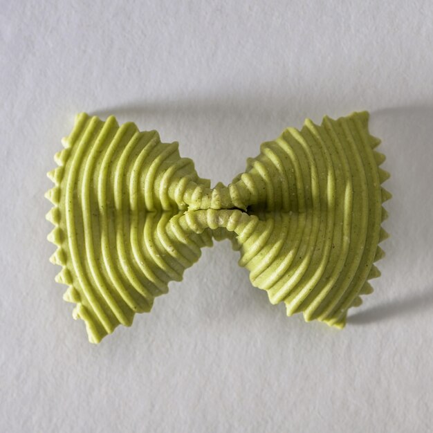 Colored bow tie pasta. Closeup single green farfalle on gray background.