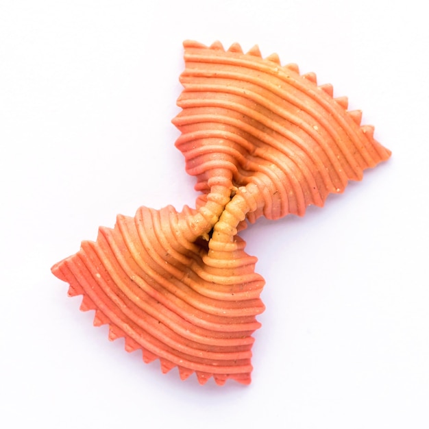 Colored bow tie pasta. Closeup single orange farfalle isolated.