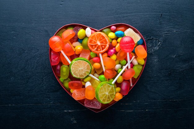 Colored candies sweets and lollipops On a black wooden background Top view Free space