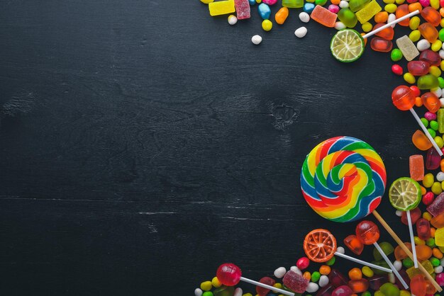 Colored candies sweets and lollipops On a black wooden background Top view Free space