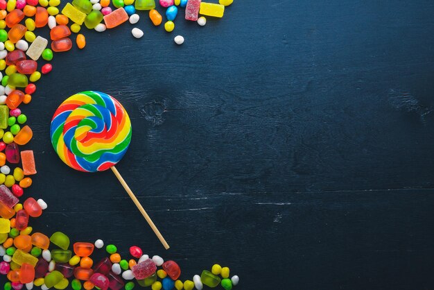 Colored candies sweets and lollipops On a black wooden background Top view Free space