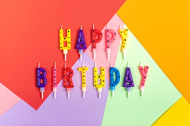 Photo colored candles on cake in the form of letters happy birthday on colorful