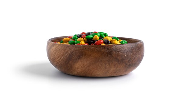 Colored chocolate sunflower seeds in wooden bowl isolated.