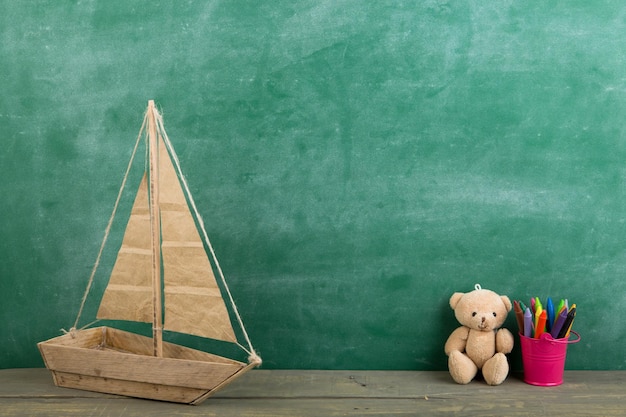 Фото Цветные мелки и игрушечный медведь на деревянном столе концепция образования начальной школы на фоне классной доски