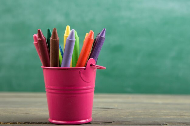 Colored crayons and toy bear on the wooden table elementary school education concept chalkboard background