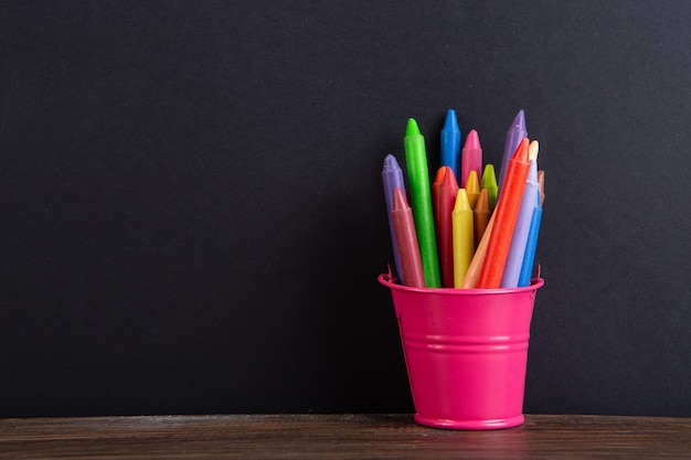 Colored crayons on the wooden table blackboard background