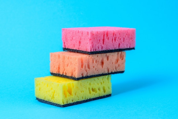 Colored dishwashing sponges are arranged in steps on a blue background.