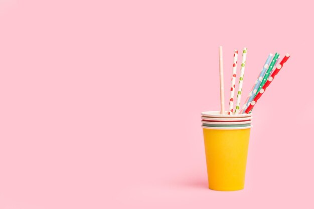 Photo colored drinking straws in colored paper glasses on a pink background with copy space