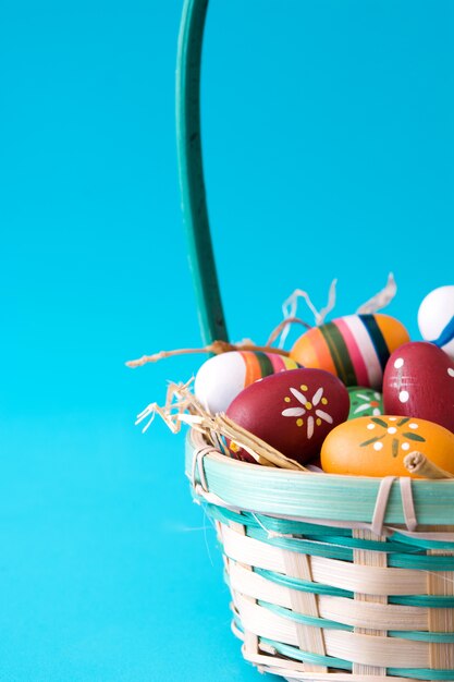 Colored easter eggs in a basket on blue surface