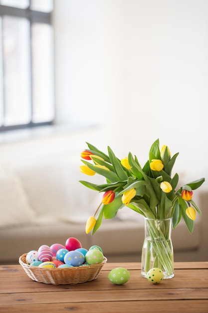 colored easter eggs in basket and flowers at home