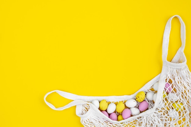 사진 노란색 배경에 있는 메쉬 백에 있는 색색의 부활절 달걀은 평평하게 놓여 있습니다.