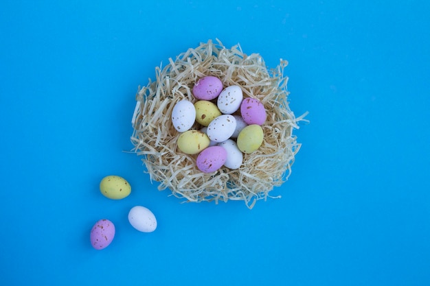 Colored easter eggs in a nest of straw on the blue background Top view Copy space