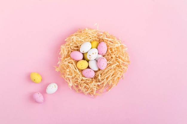 Colored easter eggs in a nest of straw on the pink background Closeup Top view