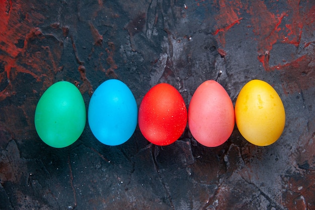 Разноцветные яйца, сложенные бок о бок на темном фоне проблемных цветов со свободным пространством