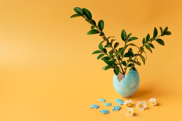 Colored eggs with spring green grass and flowering tree branch on an orange background Easter holiday family traditions