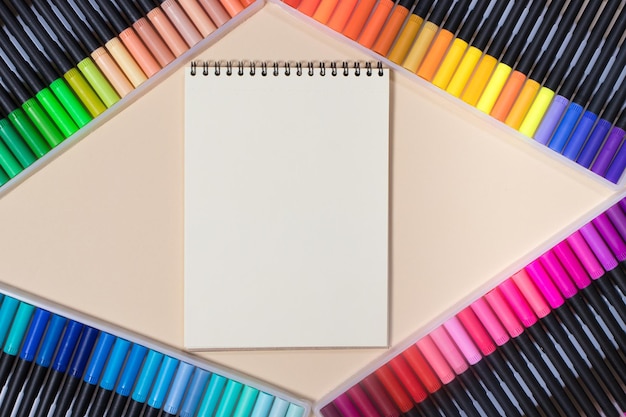 Colored felttip pens and a notebook on a beige background