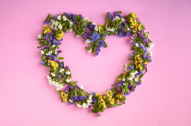 Photo colored flowers on pink surface, heart shape.