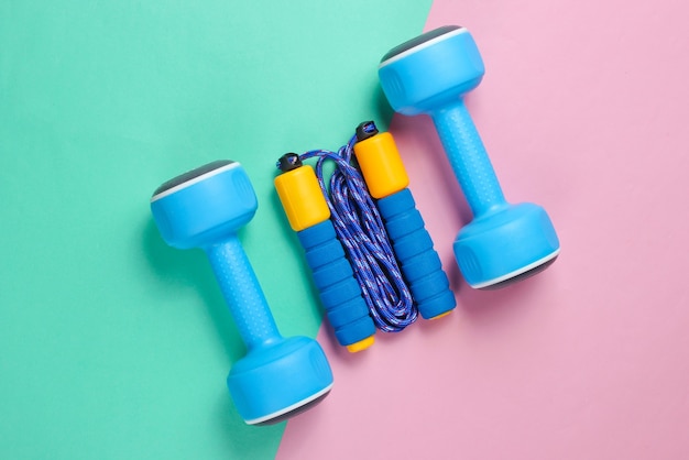 Colored jumping rope, dumbbells on a pink-blue pastel background. Minimalism sport concept.